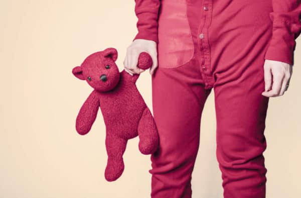 Un joven en pijama sosteniendo un osito de peluche.
