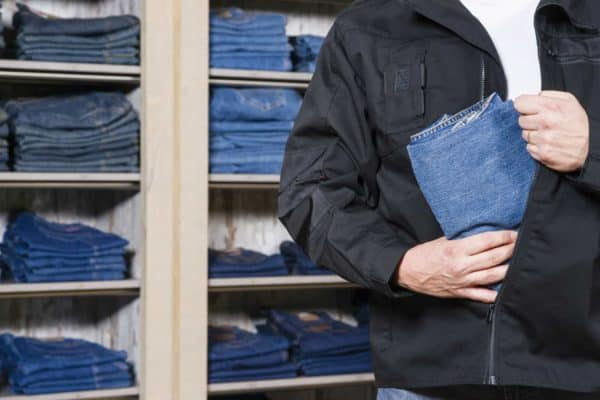 California Laws Against Organized Theft: 490.4 (PC) 1 A man puts jeans in his jacket to illustrate organized retail theft laws in California